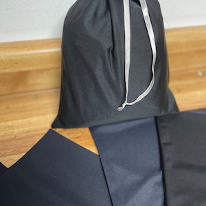 May include: A black drawstring bag with a white drawstring. The bag is sitting on a wooden surface.