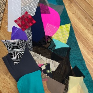 May include: A collection of fabric scraps in various colors, patterns, and textures, including black, white, green, pink, red, and blue. The fabrics are arranged on a wooden surface.