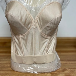 May include: A beige strapless bra with a satin finish and a lace trim. The bra has a hook and eye closure in the back.