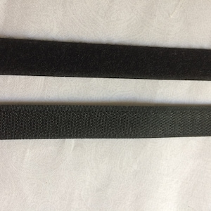 May include: Two strips of black hook and loop fastener tape. The top strip has a soft, fuzzy texture, while the bottom strip has a rough, textured surface.