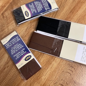 May include: Three packages of double fold quilt binding bias tape. The packages are brown, black, and white with black text. The text on the packages reads "Double Fold Quilt Binding Bias Tape" and "Ruban de Biais Double Pour Bordure de Couette".