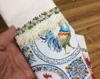May include: White kitchen towel with a rooster and floral pattern. The towel has a lace trim and a green, pink, and blue embroidered trim.