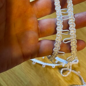 May include: White elastic trim with loops for sewing. The trim is made of a soft, flexible material and has a delicate, decorative design.
