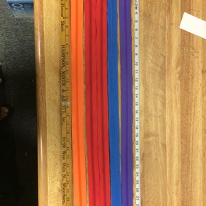 May include: Five different colored zippers, all approximately 18 inches long. The zippers are orange, red, blue, purple, and a lighter shade of blue. The zippers are laid out on a wooden surface with a ruler next to them.