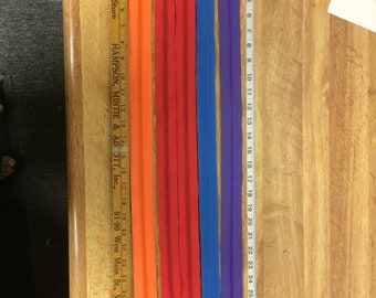 May include: Five different colored zippers, all approximately 18 inches long. The zippers are orange, red, blue, purple, and a lighter shade of blue. The zippers are laid out on a wooden surface with a ruler next to them.