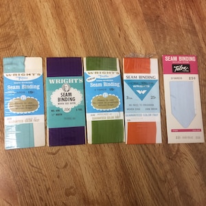 May include: Five packages of seam binding tape, each with a different color. The packages are labeled with the brand name "Wright's" and the text "Seam Binding". The colors are blue, purple, green, orange, and light blue.
