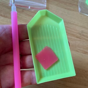May include: A green diamond painting tray with a pink wax pad and a pink diamond painting pen.