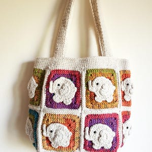 May include: A crochet tote bag constructed from multicolored granny squares, each featuring a raised, white, three-dimensional elephant motif with a small black bead eye. The bag has a cream-colored top border and two matching cream-colored handles.