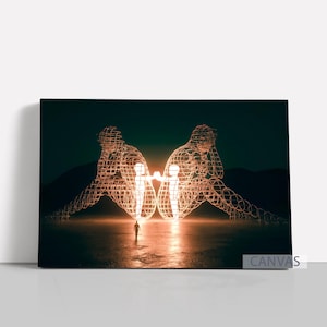 May include: Canvas art print featuring two large, illuminated wireframe figures facing each other, with a small person standing between them. The figures are in a seated position, with their heads resting on their hands. The background is a dark, moody landscape.