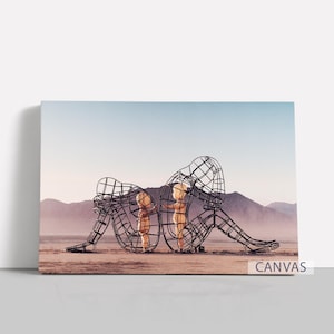 Pu&ograve; includere: Stampa su tela con due sculture a filo di figure sedute, schiena contro schiena, in un paesaggio desertico. Le sculture sono scure, con un interno chiaro. Montagne e cielo blu fanno da sfondo. La parola "CANVAS" &egrave; stampata in basso a destra.