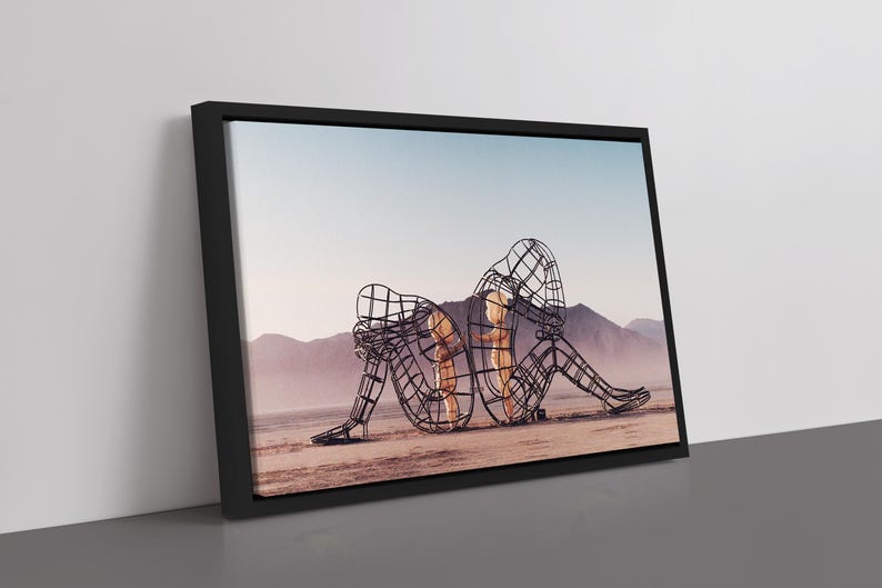 Pu&ograve; includere: Stampa artistica incorniciata raffigurante una scultura di due figure intrecciate, costruite con un design a filo metallico, ambientata in un paesaggio desertico con montagne e un cielo azzurro pallido. L'opera &egrave; incorniciata in nero.
