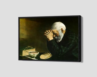 Puede incluir: Pintura enmarcada que representa a una persona mayor con barba y pelo blanco, con las manos juntas en oración. Un libro, un cuenco y pan están sobre una mesa. La persona lleva una chaqueta a cuadros verde oscuro. El fondo es oscuro.