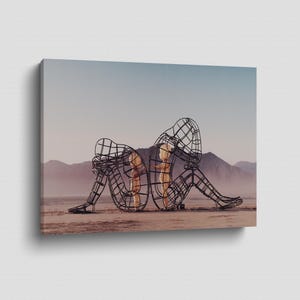 Pu&ograve; includere: Stampa su tela raffigurante due sculture a filo di figure sedute, schiena contro schiena. Le sculture sono ambientate in un paesaggio desertico con montagne e un cielo velato. Le figure sono riempite di una calda luce dorata.