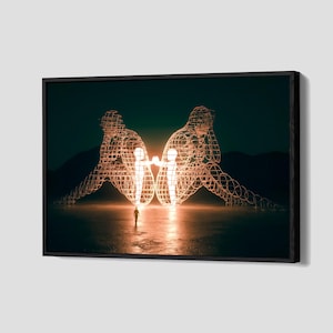 May include: A framed art print featuring two large, illuminated wireframe figures facing each other, with a small figure standing between them. The artwork has a dark, moody background with a warm, glowing light source.