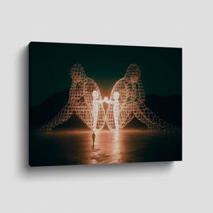 May include: A canvas print featuring a surreal landscape. Two large, wireframe figures are illuminated, each cradling a smaller figure. A lone person stands in the foreground, with a dark, moody sky and mountains in the background.
