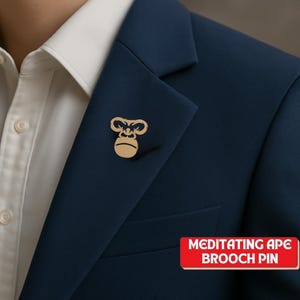 May include: A gold-colored brooch pin in the shape of a gorilla's face is pinned to a navy blue blazer. The pin is centered on the blazer's lapel. The text "MEDITATING APE BROOCH PIN" is in a red rectangle in the lower right corner.
