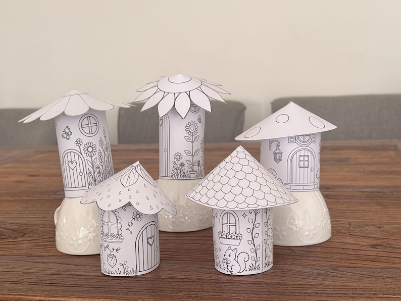 Puede incluir: Cinco casas de hadas de papel sin colorear con varios dise&ntilde;os de techo, incluyendo una flor, una seta y una fresa. Cada casa presenta un detallado dibujo lineal de puertas, ventanas y detalles florales, sobre bases de cer&aacute;mica blanca.
