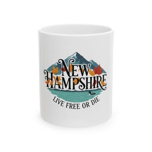 May include: White ceramic mug featuring a design with the text "New Hampshire" above a mountain and lake scene with fall leaves. The text "Live Free or Die" is below the scene.