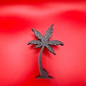 May include: A black, 3D-printed palm tree figurine. The tree has a curved trunk and a detailed frond design. The figurine is set against a bright red background, creating a striking contrast. The palm tree is a decorative item.