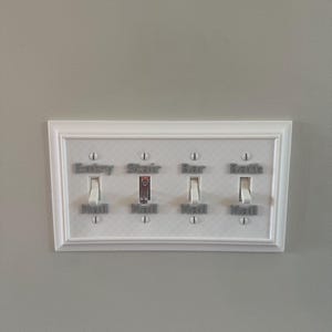 Könnte beinhalten: Eine weiße Lichtschalterplatte mit vier Schaltern. Jeder Schalter ist mit grauem Text beschriftet: "Entry Hall", "Stair Hall", "Bar Hall" und "Bath Hall". Die Platte ist an einer hellgrauen Wand befestigt.