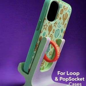 Puede incluir: Una funda de teléfono verde menta con un patrón de desierto de cactus y estrellas se muestra en un soporte a juego. El soporte tiene un bucle rojo para sujetar el teléfono. El texto en el soporte dice "For Loop & PopSocket Cases."