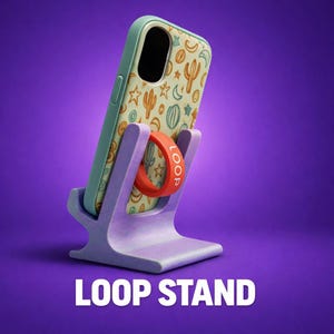 May include: A light purple phone stand holding a smartphone with a light-colored case featuring a pattern of orange and blue cacti, stars, and moons. A bright orange circular ring with the word LOOP printed in white is attached to the phone case.