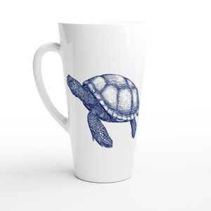 Könnte beinhalten: Weißer Keramik-Latte-Becher mit einer blauen Illustration einer Meeresschildkröte. Die Schildkröte ist mit detaillierten Linien dargestellt, die ihre Textur hervorheben. Der Becher hat eine hohe, schlanke Form und einen gebogenen Griff.