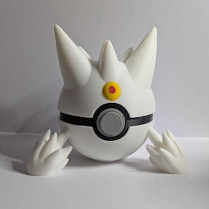 Puede incluir: Una figura de Togepi blanca, impresa en 3D, con cuerpo redondo, cabeza puntiaguda y pequeños apéndices en forma de alas. La figura tiene una banda negra en el centro y un ojo amarillo con centro rojo. Es un objeto de colección.