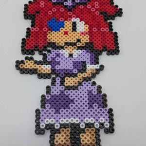 May include: A pixel art figure of a girl made from colorful plastic beads. The figure has red hair, a purple dress, and brown shoes. The figure is set against a white background.