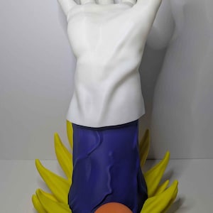 May include: A white hand statue with a blue and yellow base, and an orange ball with a red star. The hand is in a gesture of power, with the fingers extended. The base is a stylized flame design.