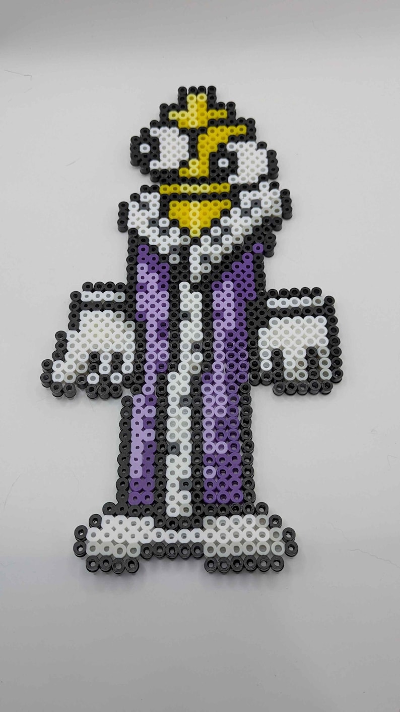 May include: A pixel art figure of a character in a purple and white outfit with a yellow crown. The figure is made of small, colorful beads, with black beads outlining the design. The figure has a white beard and mustache.