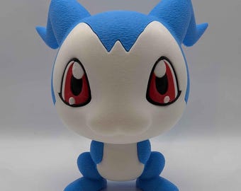 Puede incluir: Una pequeña figura de criatura estilizada con un cuerpo azul texturizado y una cara blanca lisa. La figura presenta grandes ojos rojos en forma de almendra con reflejos blancos, orejas puntiagudas a los lados y una postura compacta.