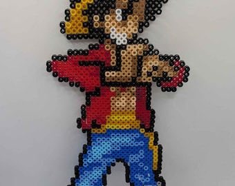Puede incluir: Representación en pixel art de un personaje de la serie de anime One Piece. La figura, hecha de cuentas de colores, lleva un sombrero de paja amarillo, una chaqueta roja, pantalones cortos azules y zapatos negros. El personaje está en una pose dinámica.