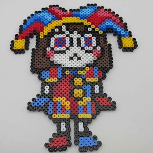 May include: A colorful jester figure crafted from fused plastic beads. The jester has a white face, brown hair, and wears a red and blue outfit with yellow accents. The jester's hat is a vibrant mix of red, blue, and yellow.