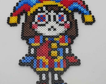 Puede incluir: Una figura de bufón colorida hecha de cuentas de plástico fusionadas. El bufón tiene una cara blanca, cabello castaño y viste un atuendo rojo y azul con detalles amarillos. El sombrero del bufón es una mezcla de rojo, azul y amarillo.