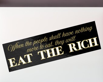May include: A white laptop with a black sticker that reads "When the people shall have nothing more to eat, they will EAT THE RICH" in gold lettering. The laptop is on a white desk.