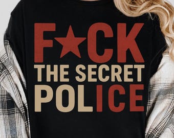 May include: Black t-shirt with the text "F*CK THE SECRET POLICE" in red and tan lettering. The word "F*CK" has a red star replacing the letter "A". The shirt is worn with a plaid button-down shirt.