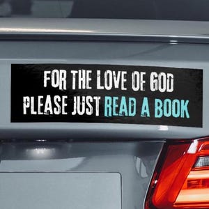 May include: A rectangular bumper sticker with the text "FOR THE LOVE OF GOD PLEASE JUST READ A BOOK" in white and teal lettering on a black background. The sticker is attached to the rear of a grey car.