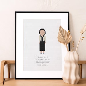 May include: A framed print with a pixelated illustration of Coco Chanel, a famous fashion designer, wearing a white jacket and black skirt. The quote "Simplicity is the keynote of all true elegance." is printed below the illustration, attributed to Coco Chanel.