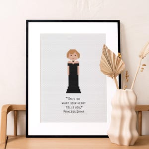May include: Framed cross-stitch art featuring a pixelated image of Princess Diana in a black dress. The quote "Only do what your heart tells you." is below the image. The artwork is in a black frame.