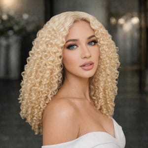May include: A person with long, blonde, curly hair and blue eyes, wearing a white, off-the-shoulder top. The background is blurred, with soft lighting, creating a soft focus portrait.