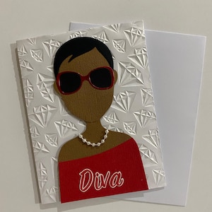 May include: A handmade greeting card featuring a stylized illustration of a person wearing red sunglasses and a pearl necklace. The card has a red top with the word "Diva" and a white diamond pattern.
