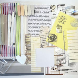 May include: A stationery set including a mesh pencil case with colorful stripes, various pens, adhesive tabs, a library card bookmark, a clear clip, a heart-shaped cutout, washi tape rolls, and several sheets of paper featuring printed inspirational text.