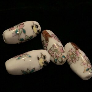 May include: Four white ceramic beads with floral and bird designs in pink, green, gold, and brown.