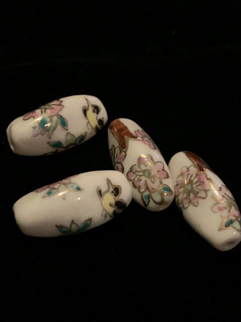 May include: Four white ceramic beads with floral and bird designs in pink, green, gold, and brown.
