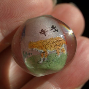 May include: A clear glass bead with a painted image of a leopard and Chinese characters. The bead has a slight iridescent sheen.