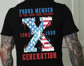 May include: Black t-shirt with a graphic design featuring a large "X" composed of the American flag and stars. Text includes "PROUD MEMBER," "GENERATION," and the years 1965 and 1980, in red and blue.