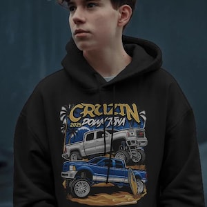 May include: Black hooded sweatshirt featuring a graphic of two lifted trucks with the text "Cruzin Downtown 2025". The design includes palm trees and a surfboard, suggesting a beach theme. The trucks are in white and blue.