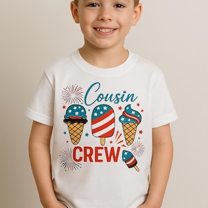 May include: A white t-shirt with a graphic design featuring ice cream cones and popsicles in red, white, and blue, with the words "Cousin Crew". The shirt is worn by a smiling child.