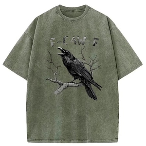May include: An olive green t-shirt with a graphic of a black raven on a branch, and the word "F-CAW-F" above. The tee has a vintage, washed appearance.